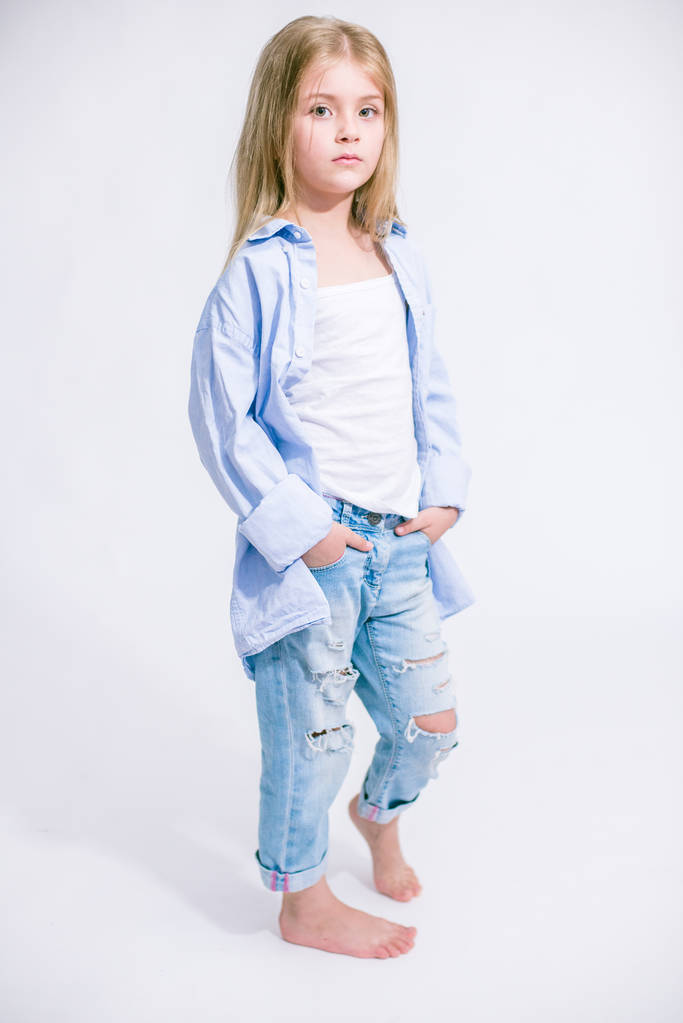 Sarı saçlı beyaz bir arka planda Studio kot pantolon giysili güzel şık küçük kızla - Fotoğraf, Görsel