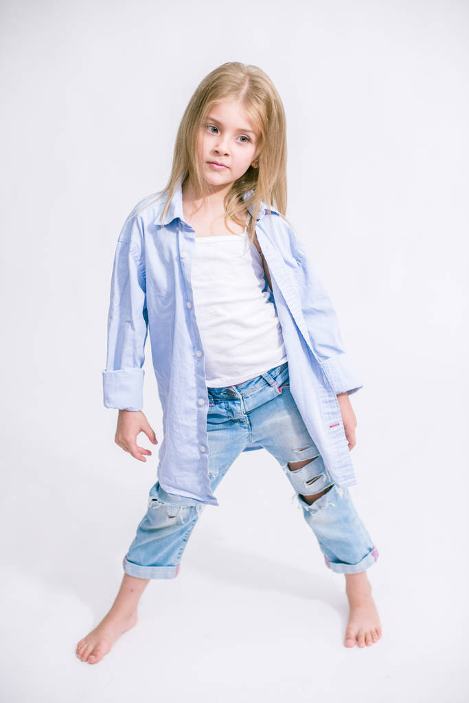 Красива модна маленька дівчинка з світлим волоссям в джинсовому одязі на білому тлі в студії
 - Фото, зображення