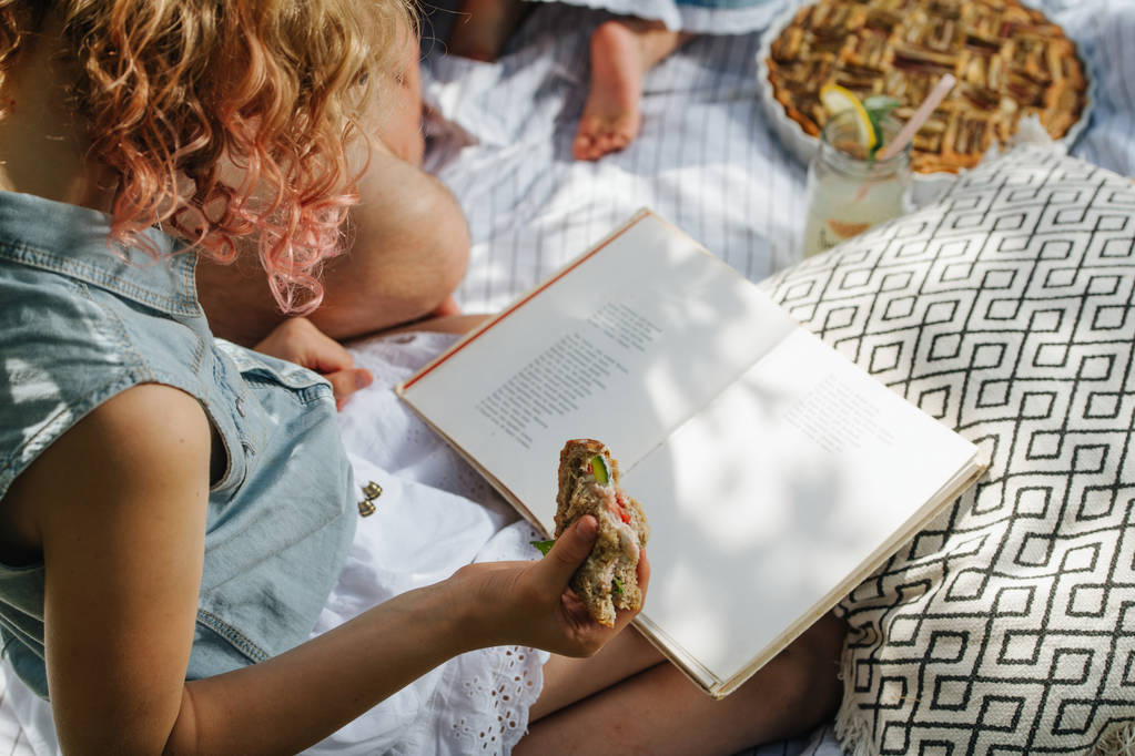 Tizenéves lány olvasás könyvet fű alatt családi piknik a kertekben - Fotó, kép