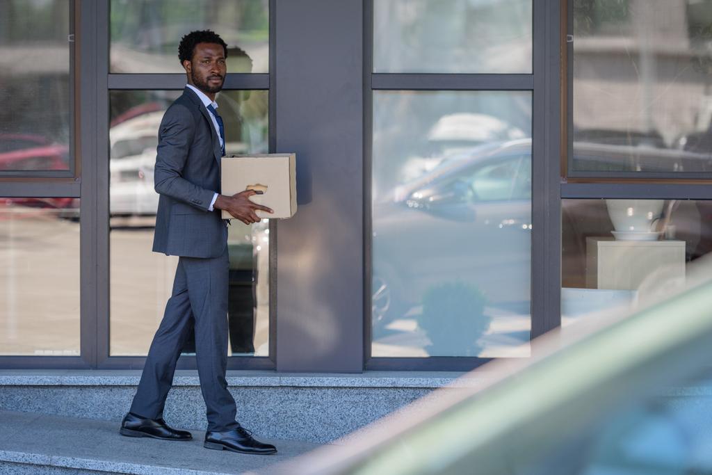 foco selectivo del empresario afroamericano despedido que lleva la caja de cartón
 - Foto, imagen