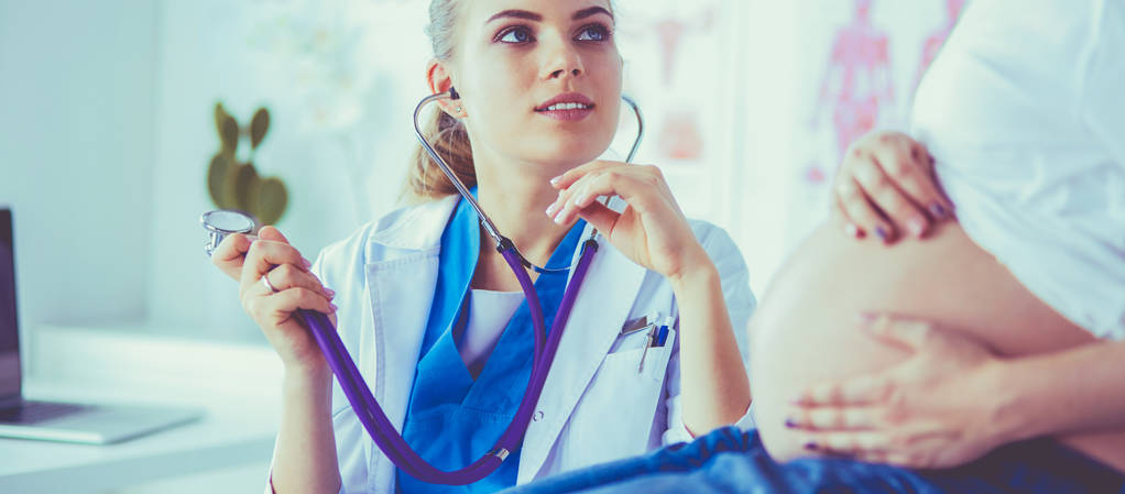 Młoda kobieta lekarz ze stetoskopem rozmawia z ciężarną kobietą w szpitalu. - Zdjęcie, obraz
