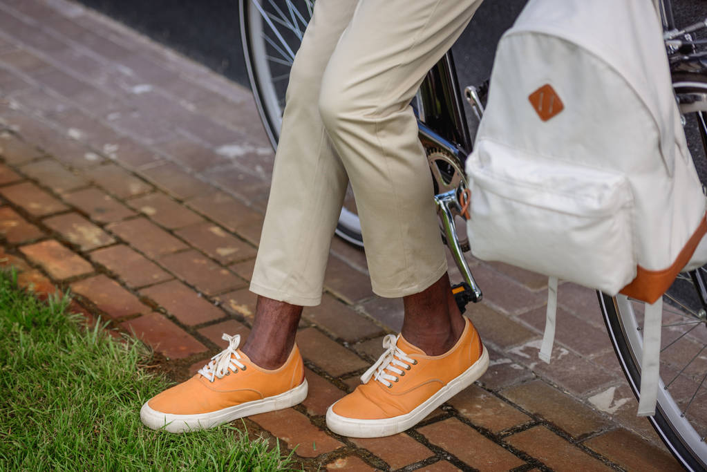 vista recortada de hombre afroamericano con estilo de pie cerca de la bicicleta con mochila
 - Foto, imagen