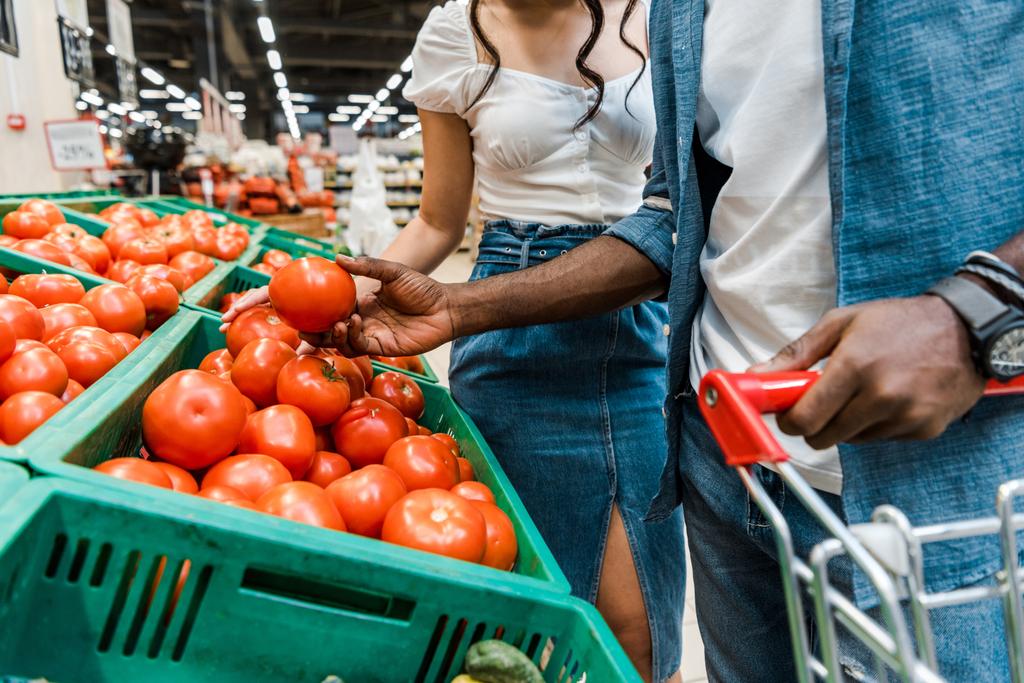 vista cortada do homem americano africano que prende o tomate fresco perto da menina no supermercado
  - Foto, Imagem