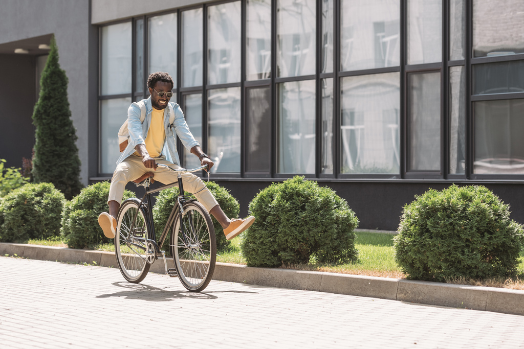 onnellinen, tyylikäs afrikkalainen amerikkalainen mies hymyilee ajaessaan polkupyörällä
 - Valokuva, kuva
