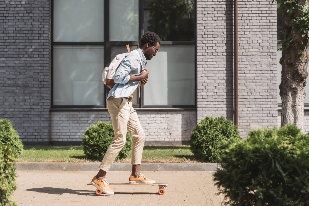 Stylowy African American Man z plecak jazda Longboard na słonecznej ulicy - Zdjęcie, obraz