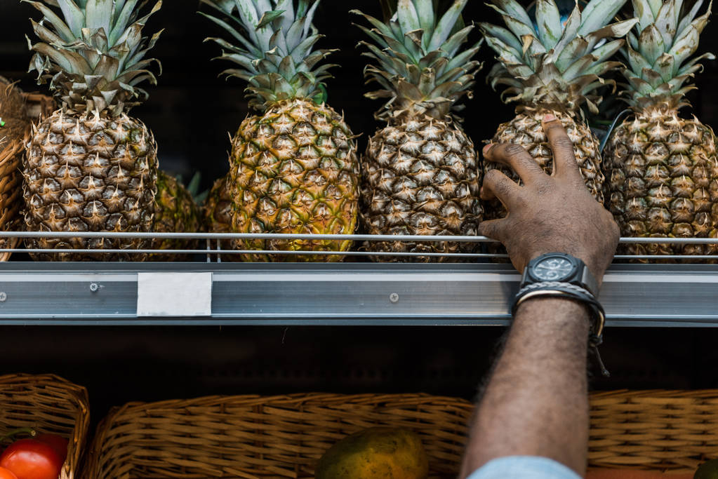 スーパーマーケットでパイナップルを取るアフリカ系アメリカ人男性のトリミングビュー  - 写真・画像
