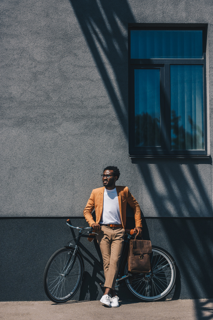 handsome, stylish african american businessman standing with bicycle near wall - Photo, Image