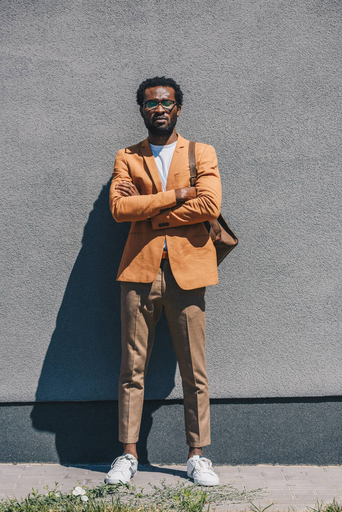 guapo, elegante hombre de negocios afroamericano de pie con los brazos cruzados por la pared en la calle
 - Foto, imagen