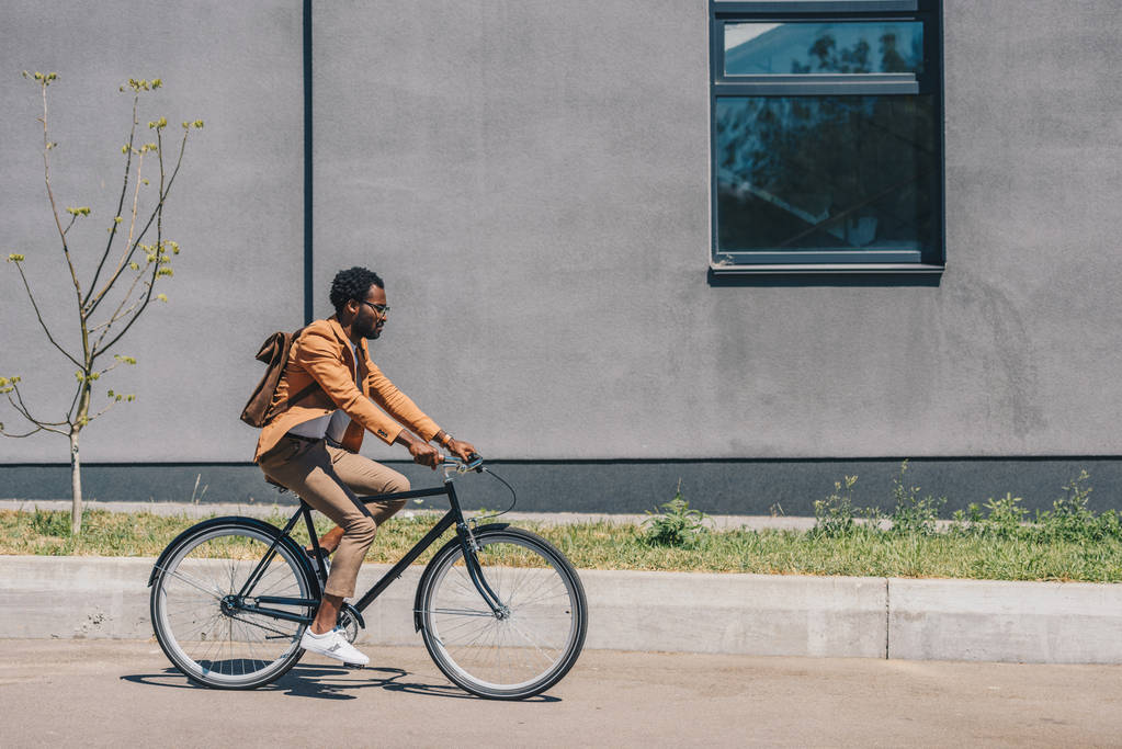 élégant homme d'affaires afro-américain à vélo sur la rue ensoleillée
 - Photo, image