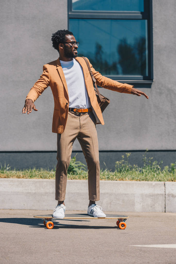 gutaussehender, stylischer afrikanisch-amerikanischer Geschäftsmann reitet Longboard auf der Straße - Foto, Bild