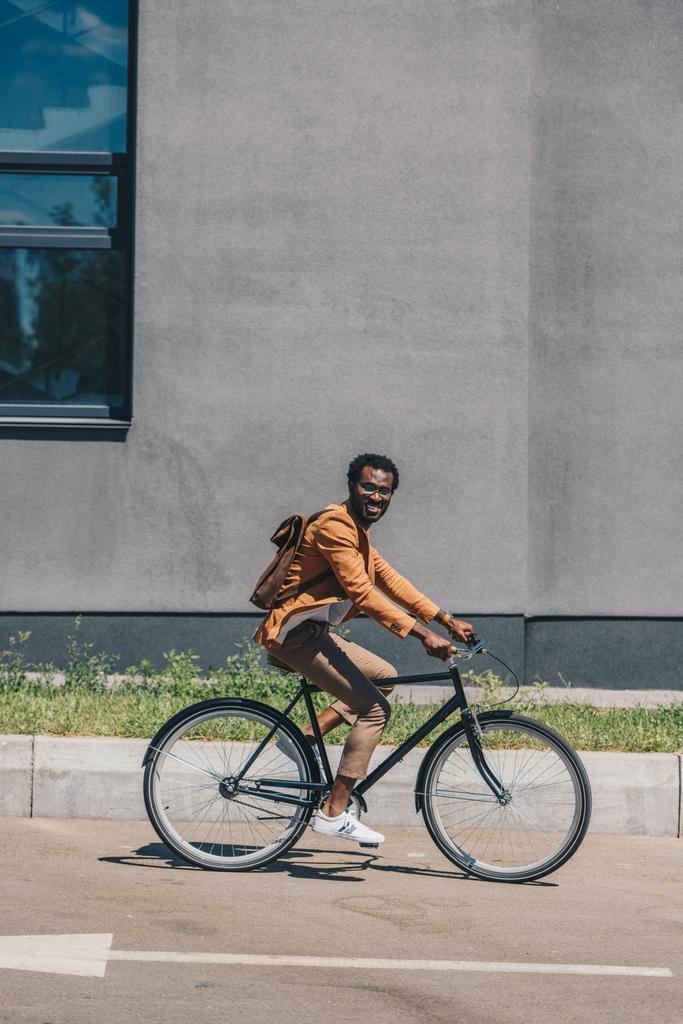 vidám afro-amerikai üzletember lovaglás kerékpár, miközben mosolyogva kamera - Fotó, kép