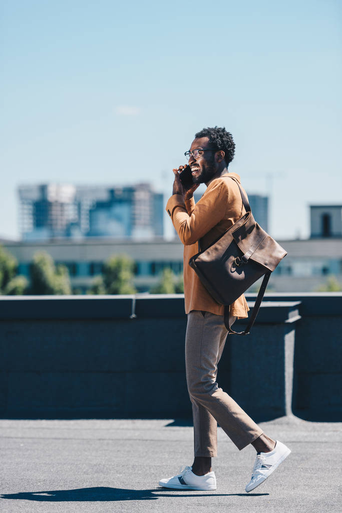 χαμόγελο Αφρικανός Αμερικανός επιχειρηματίας μιλάει στο smartphone, ενώ περπατάει στην ταράτσα - Φωτογραφία, εικόνα