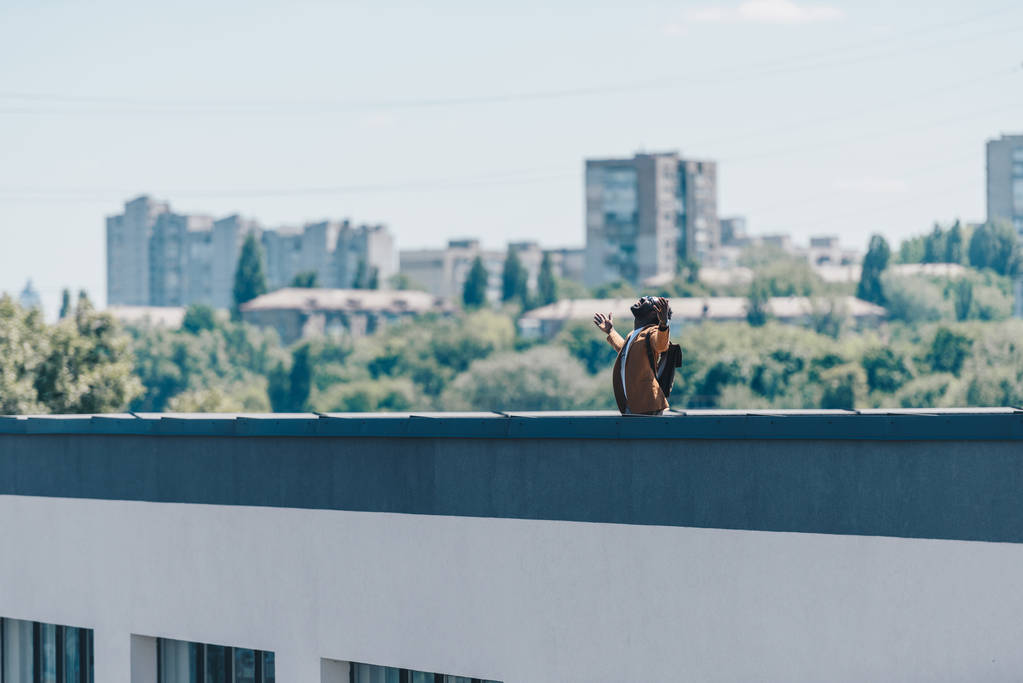 Afrikkalainen amerikkalainen mies elehtii kohotetuin käsin seistessään katolla rakennuksen
 - Valokuva, kuva