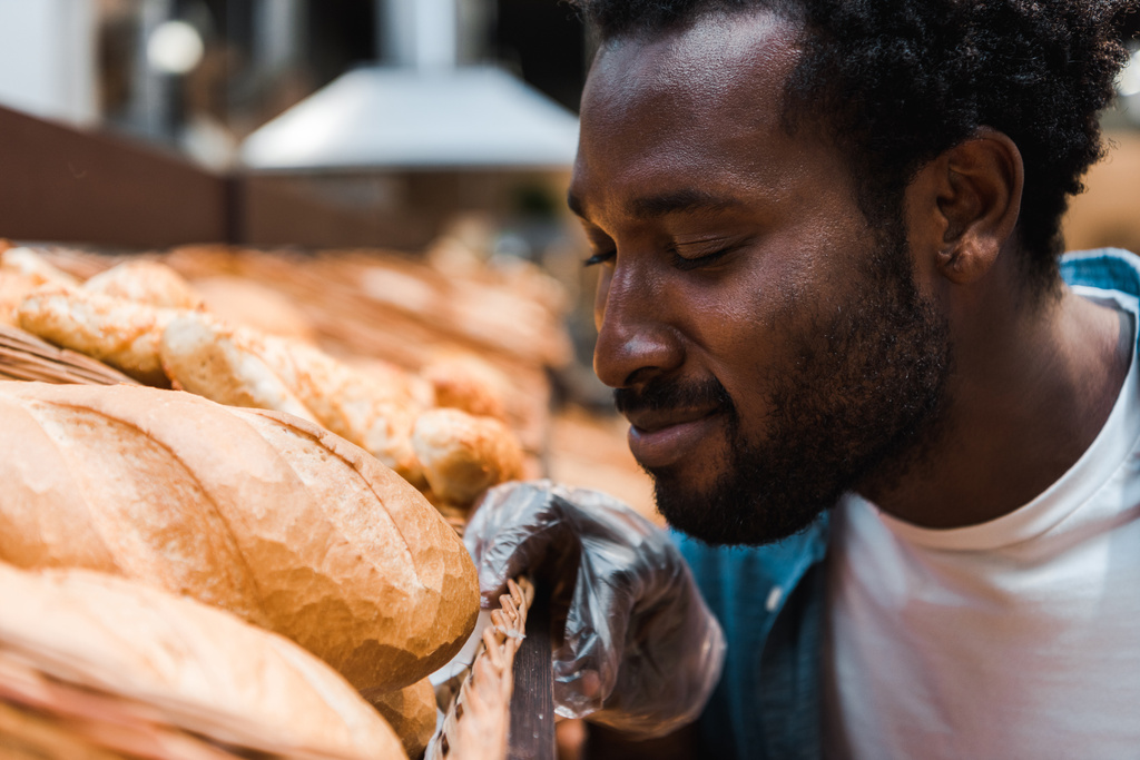 επιλεκτική εστίαση του Happy Αφρικανός Αμερικανός άνθρωπος μυρωδιά φρέσκο ψωμί στο σούπερ μάρκετ  - Φωτογραφία, εικόνα