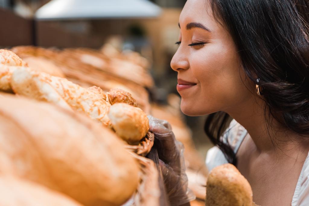 valikoiva painopiste iloinen aasialainen nainen hymyilee samalla haju leipää supermarketissa
  - Valokuva, kuva