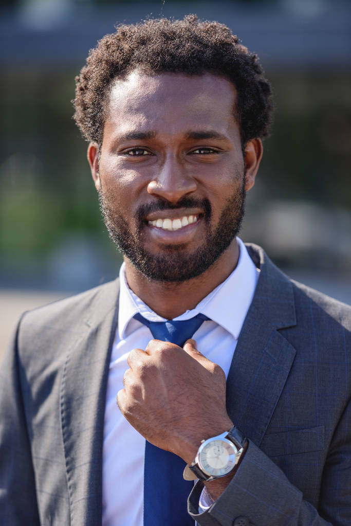 beau, joyeux homme d'affaires afro-américain touchant cravate et souriant à la caméra
 - Photo, image