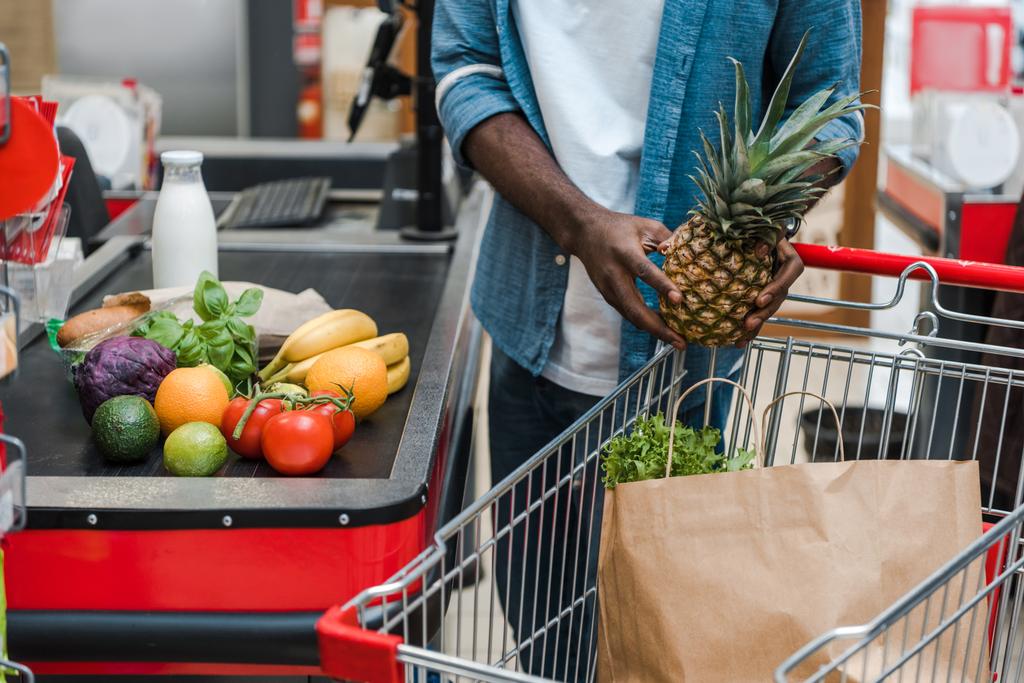 nyírt kilátás afroamerikai férfi gazdaság ananász közelében szupermarket számláló  - Fotó, kép