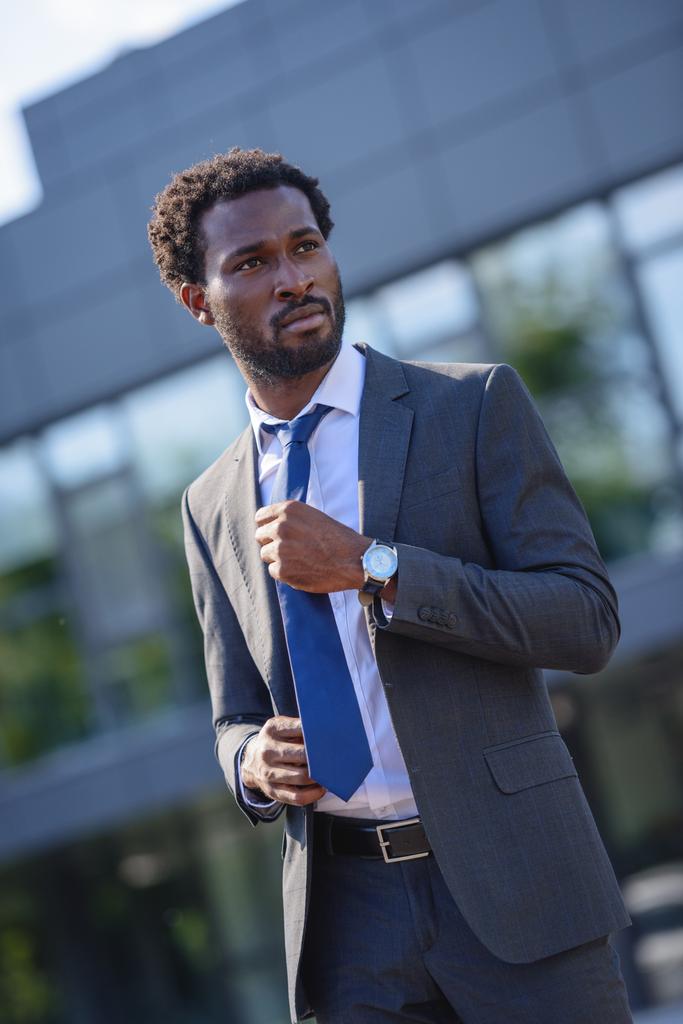 уверенный в себе африканский американский бизнесмен касаясь галстука и глядя в сторону на улице
 - Фото, изображение