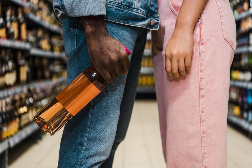 Nahaufnahme eines afrikanisch-amerikanischen Mannes mit Flasche und Wein in der Nähe einer Frau im Supermarkt  - Foto, Bild