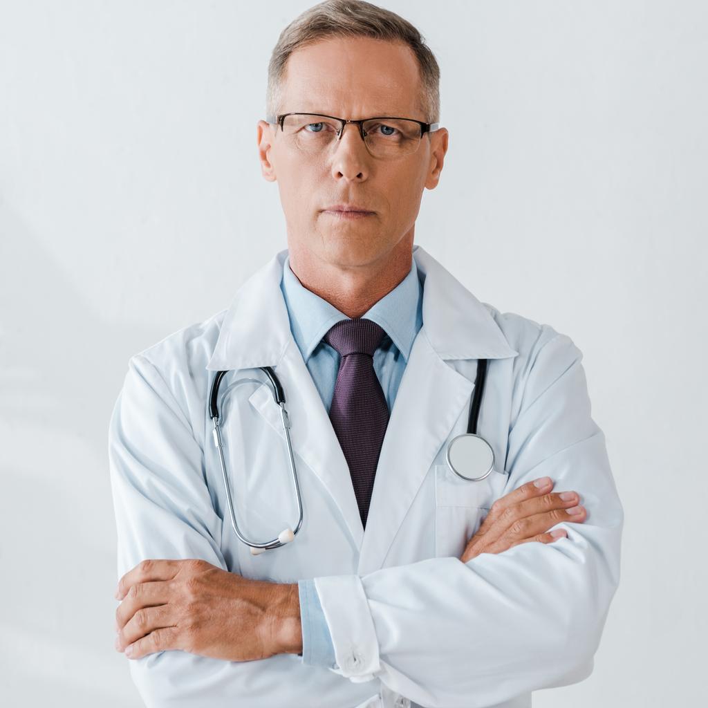 schöner Arzt mit Stethoskop, der mit verschränkten Armen vor der Kamera steht  - Foto, Bild