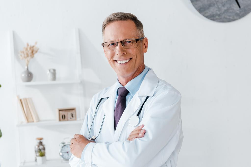 ευτυχισμένος γιατρός με λευκό παλτό και γυαλιά με σταυρωτά μπράτσα  - Φωτογραφία, εικόνα