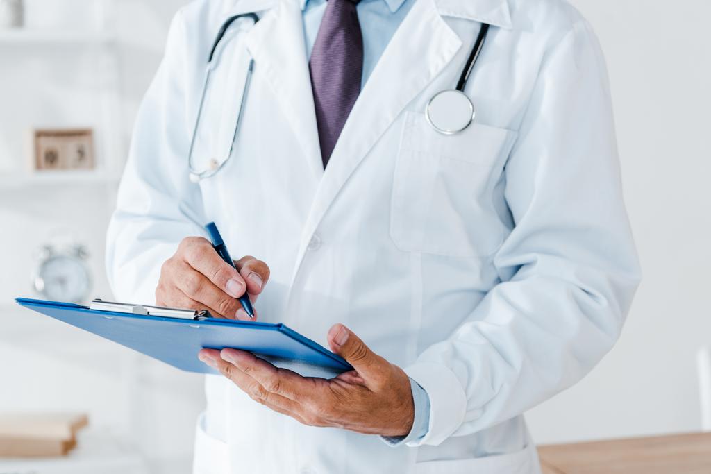 vista recortada del médico en capa blanca sujetando portapapeles y diagnóstico de escritura
  - Foto, imagen