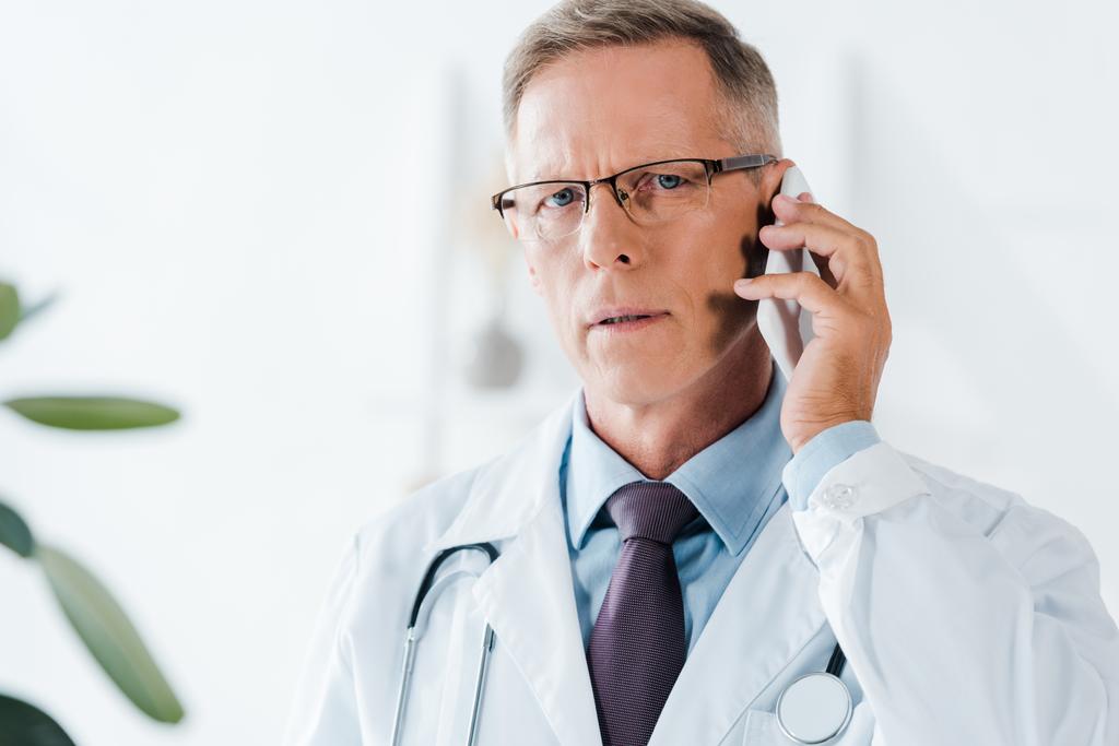 красивий лікар дивиться на камеру і розмовляє по смартфону в клініці
  - Фото, зображення