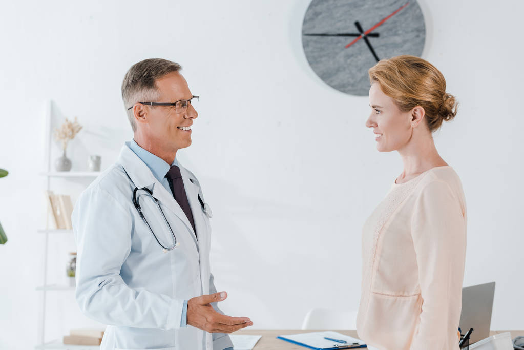 cheerful doctor gesturing while looking at attractive woman  - Photo, Image
