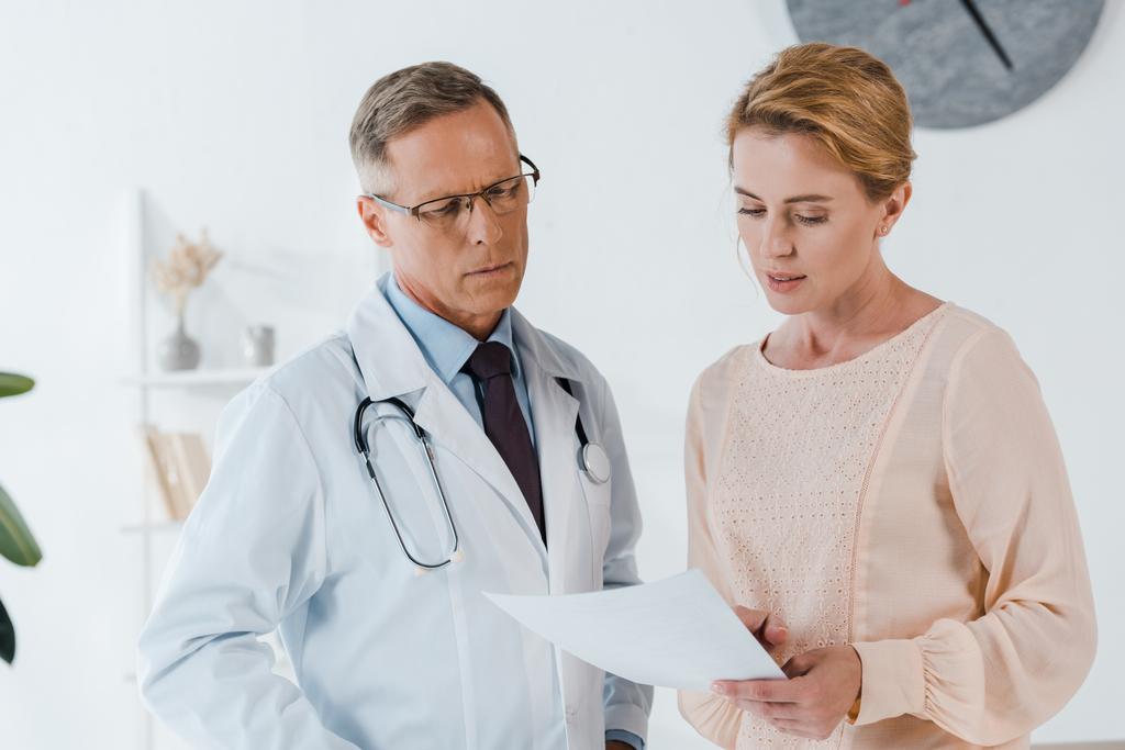 handsome doctor in glasses and woman looking at document  - Photo, Image