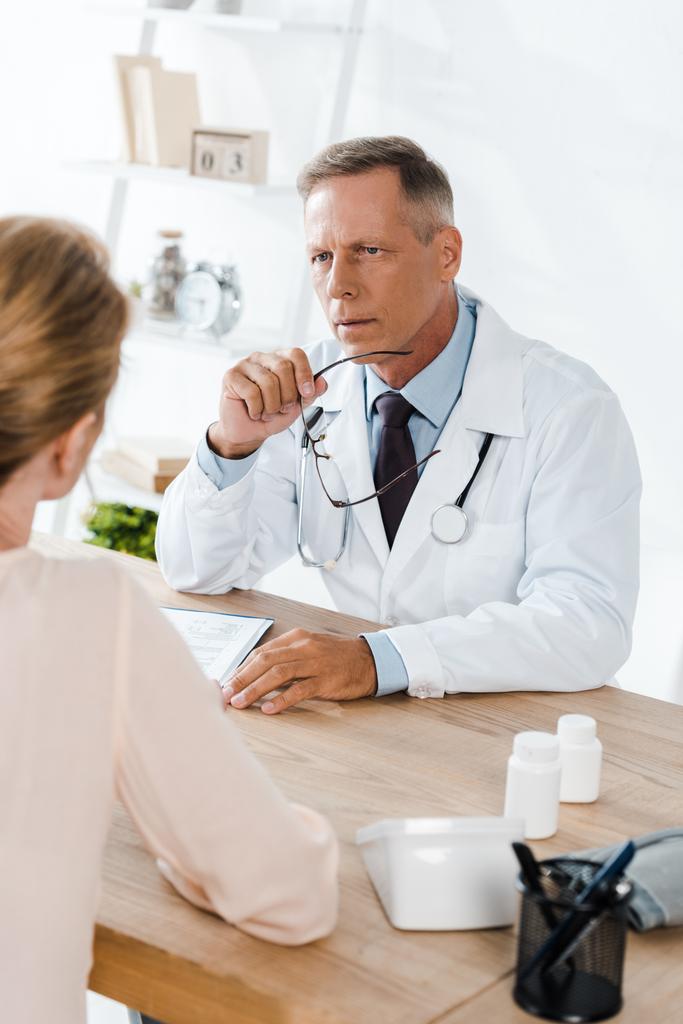 селективное внимание врача, смотрящего на женщину и держащего очки в клинике
  - Фото, изображение