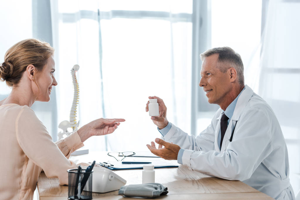 attractive woman pointing with finger at bottle near happy doctor  - Photo, Image