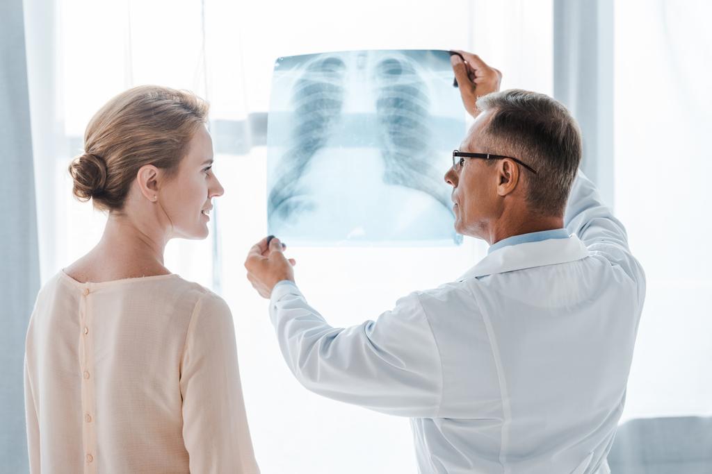 Doktor v bílém kabátě a žena se na sebe dívají blízko rentgenového paprsku na klinice  - Fotografie, Obrázek