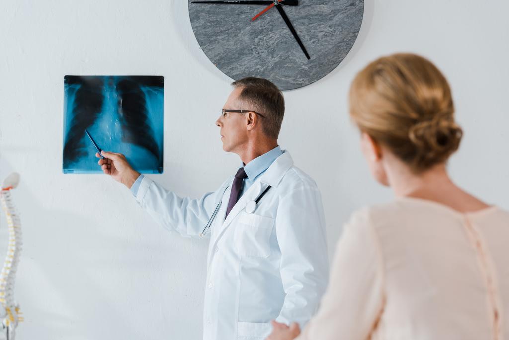 selective focus of doctor in white coat holding pen near x-ray and woman in clinic  - Photo, Image