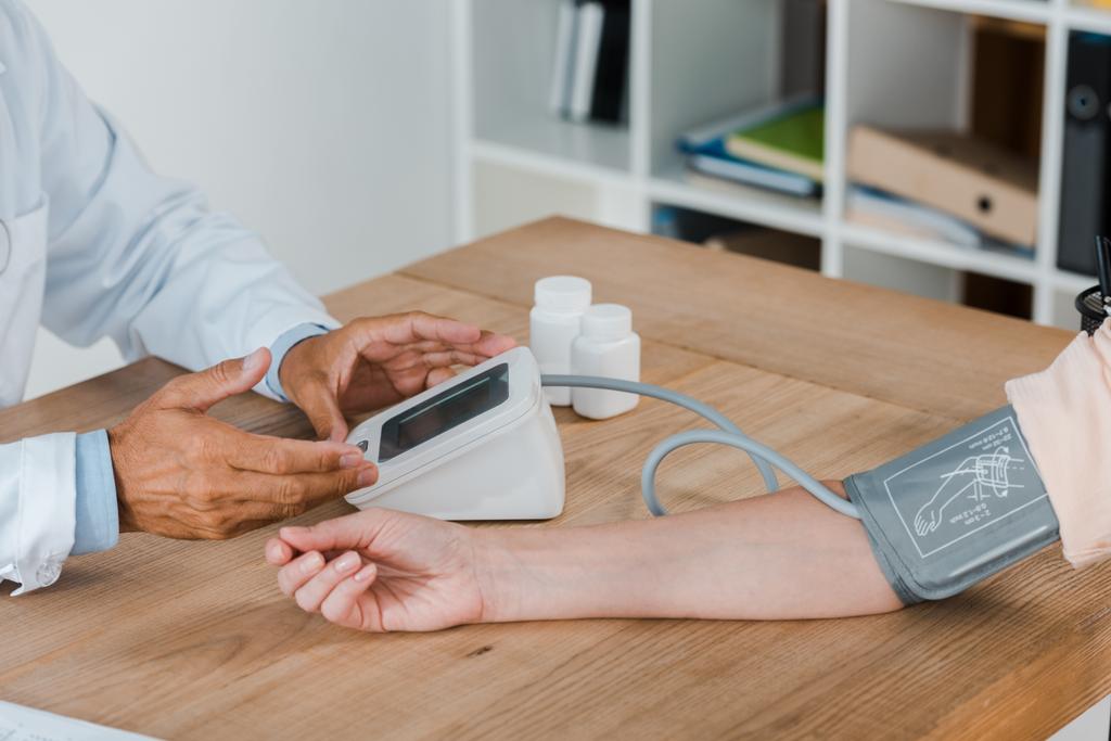 oříznutý pohled na doktorský gestikulaci při měření krevního tlaku ženy  - Fotografie, Obrázek