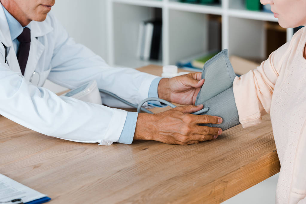 病院のテーブルの上の女性の血圧を測定する医師のトリミングビュー - 写真・画像