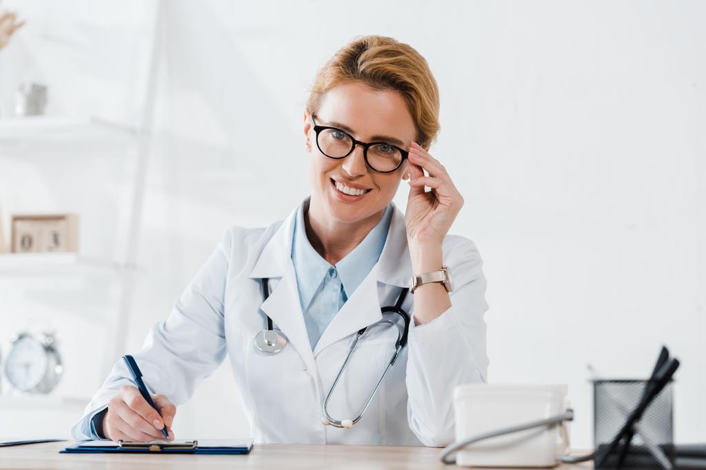 médico feliz tocando óculos e diagnóstico de escrita na clínica
  - Foto, Imagem