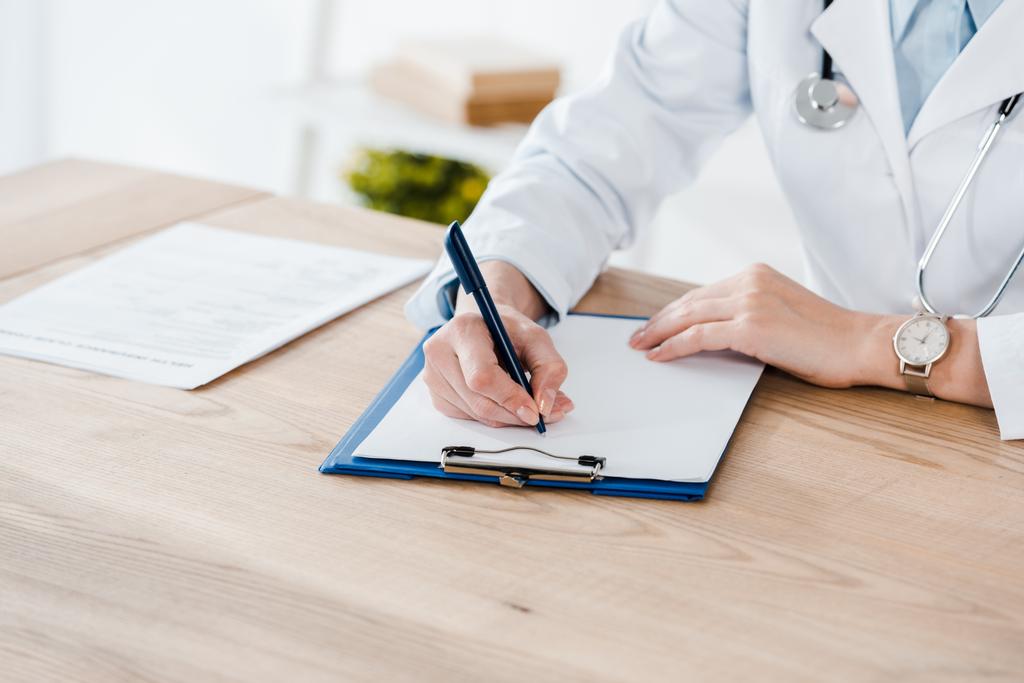 vista ritagliata del medico in camice bianco diagnosi di scrittura su tavolo di legno
  - Foto, immagini