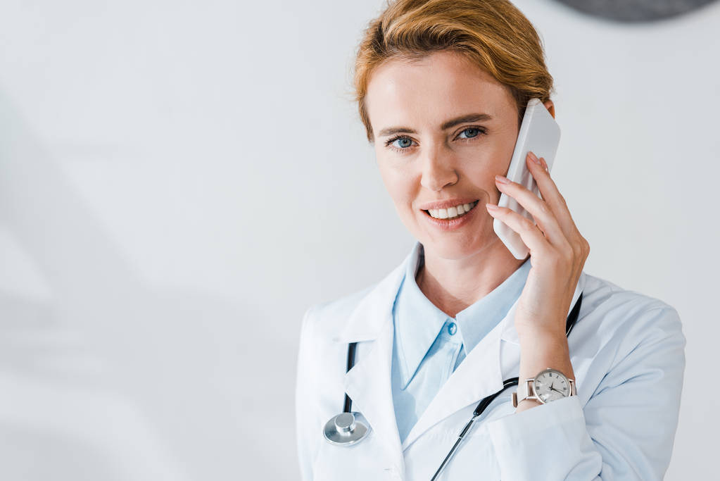 happy doctor looking at camera and smiling while talking on smartphone  - Photo, Image