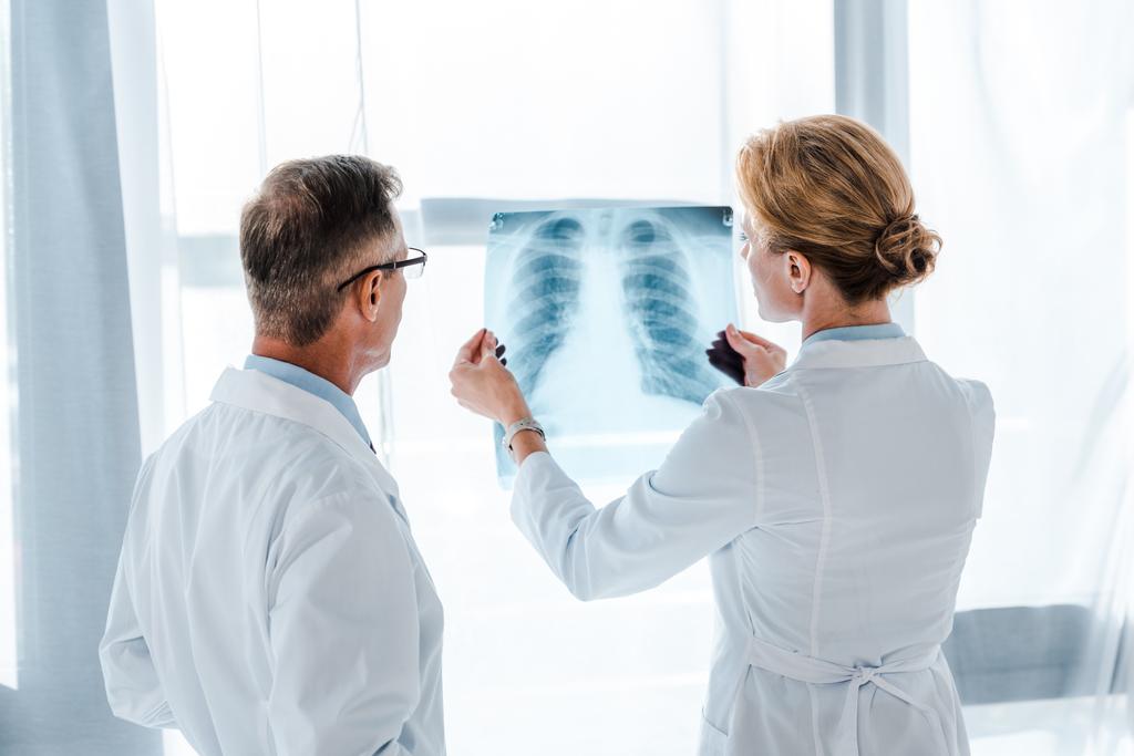 médico em óculos olhando para raio-x em mãos de colega de trabalho
  - Foto, Imagem