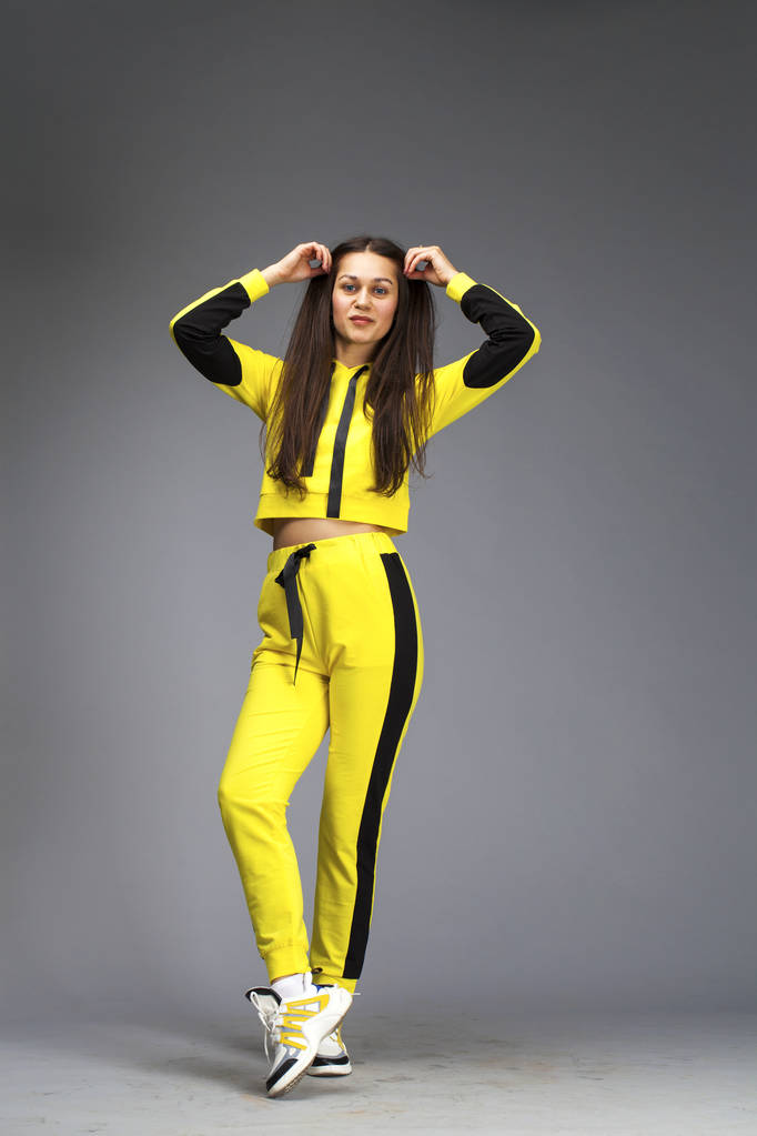 Portrait of a young beautiful brunette woman in yellow tracksuit - Photo, Image