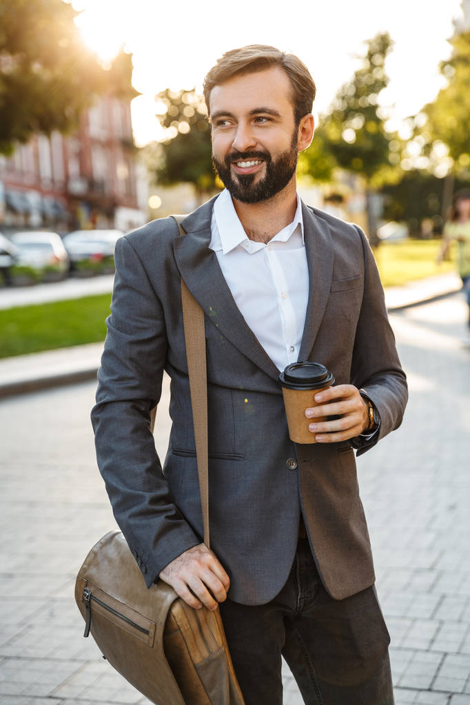 Портрет кавказского взрослого бизнесмена в формальном костюме, держащего кофе на вынос во время прогулки по городской улице
 - Фото, изображение