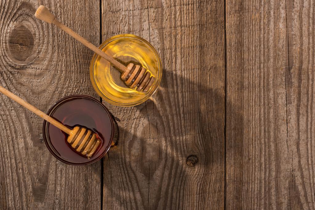 日光の下で木製のテーブルの上に蜂蜜と蜂蜜のディッパーと瓶のトップビュー - 写真・画像