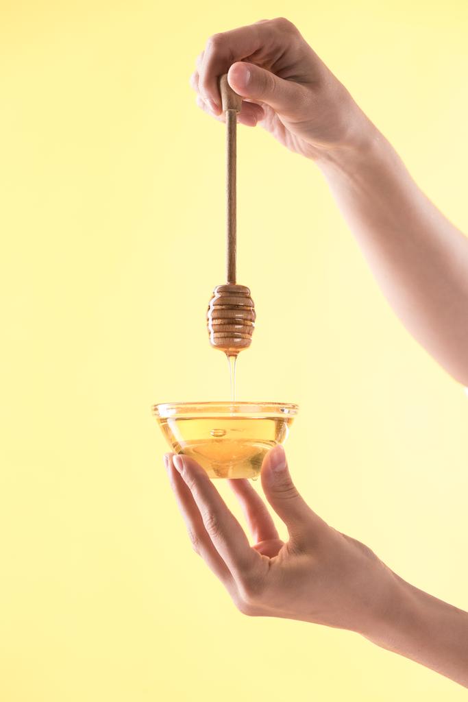 cropped view of woman holding glass bowl and wooden dipper with dripping honey isolated on yellow - Photo, Image