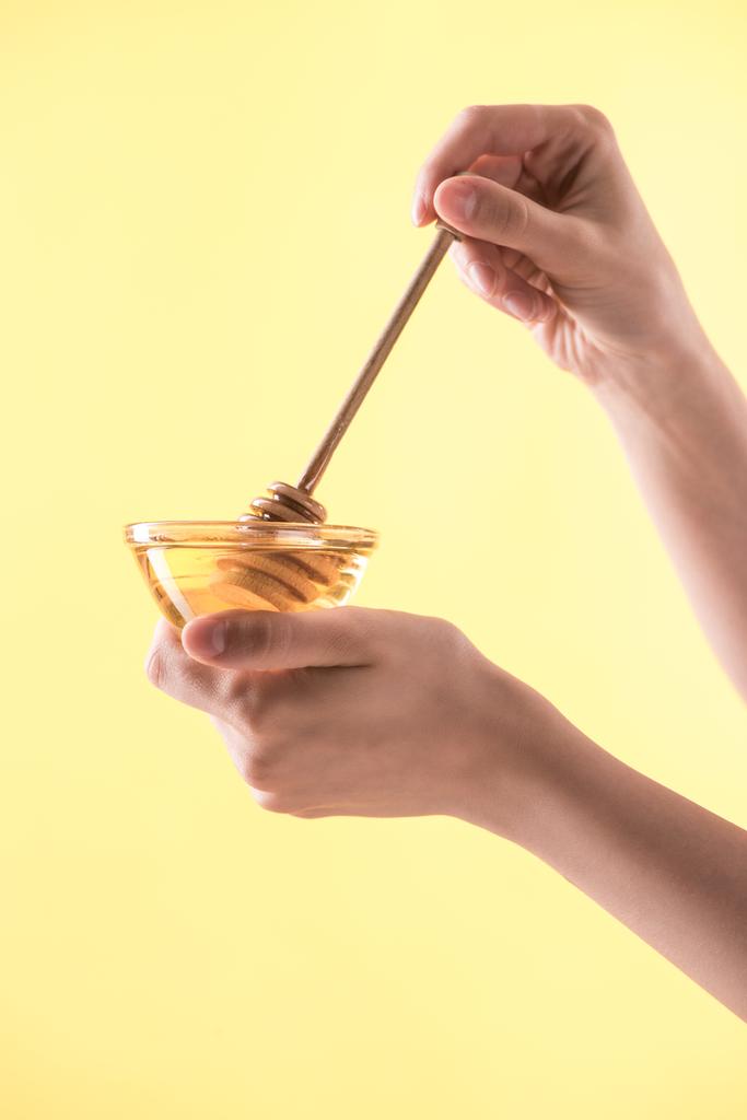 cropped view of woman holding glass bowl and wooden dipper in honey isolated on yellow - Photo, Image