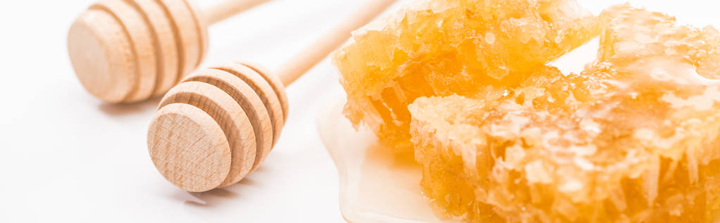 plano panorámico de panal dulce con miel cerca de bañadores de miel de madera sobre fondo blanco
 - Foto, Imagen