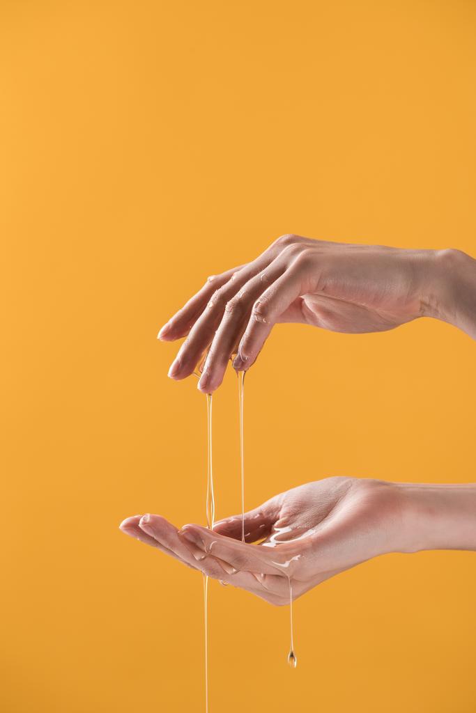 részleges tekintettel a nő mutatja kezét csöpögő mézet izolált narancs - Fotó, kép