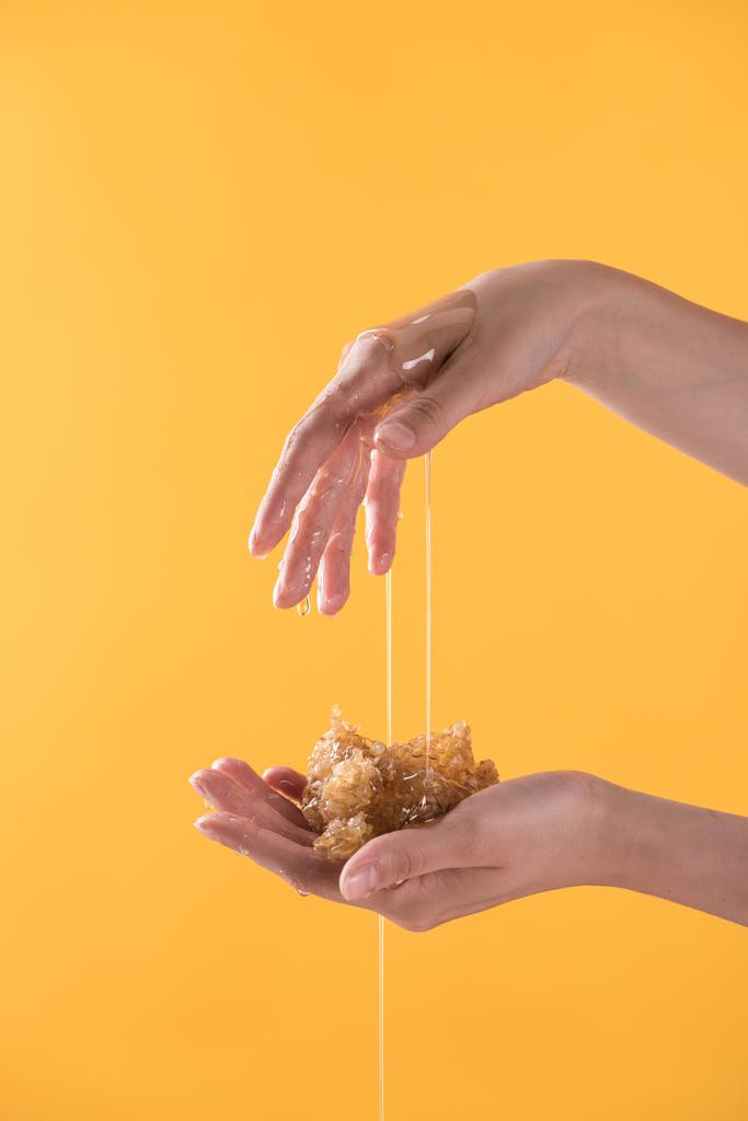 vista recortada de la mujer que muestra las manos en la miel goteando y la celebración de panal aislado en naranja
 - Foto, imagen