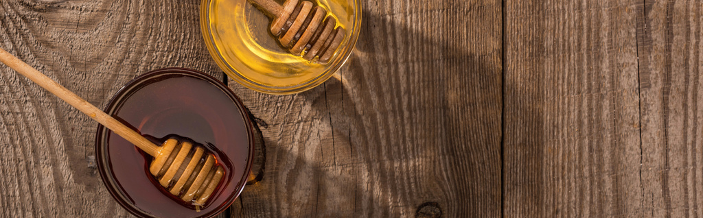 plano panorámico de tarros con bañadores de miel y miel sobre mesa de madera a la luz del sol
 - Foto, imagen