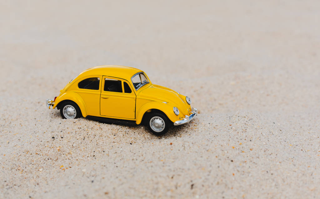 砂の自然な背景に黄色の小さな車。夏休みのコンセプト - 写真・画像