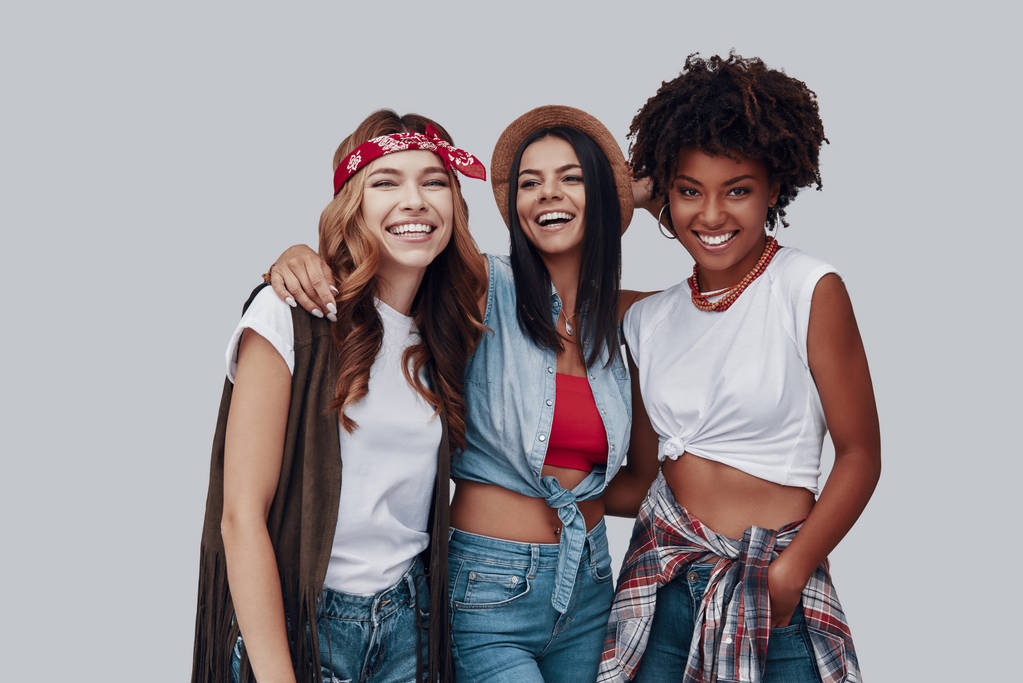 Kolme viehättävää tyylikästä nuorta naista katselee kameraa ja hymyilee seistessään harmaata taustaa vasten
 - Valokuva, kuva